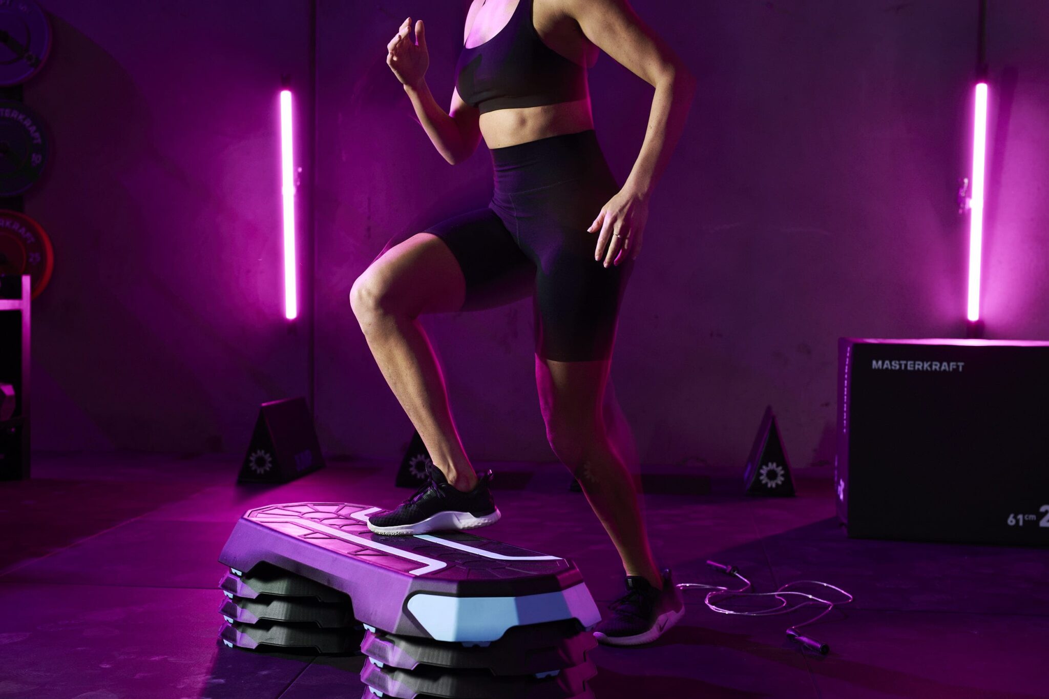 A female fitness model doing a step up wearing black tight shorts and a black crop top.